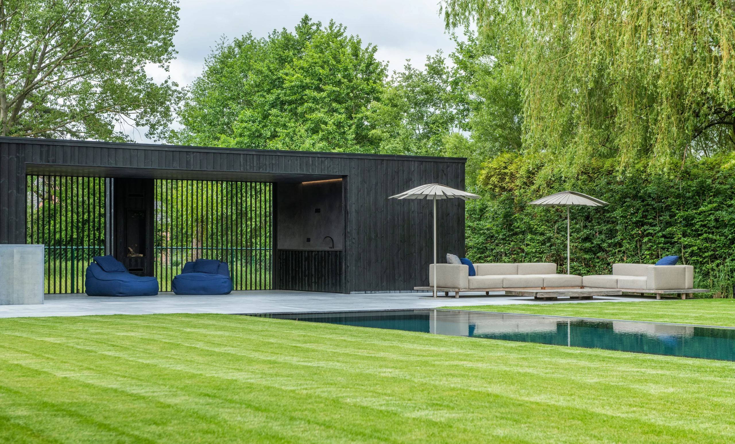 Moderne tuin met zwembad en strak bijgebouw in donkere houtstructuur.