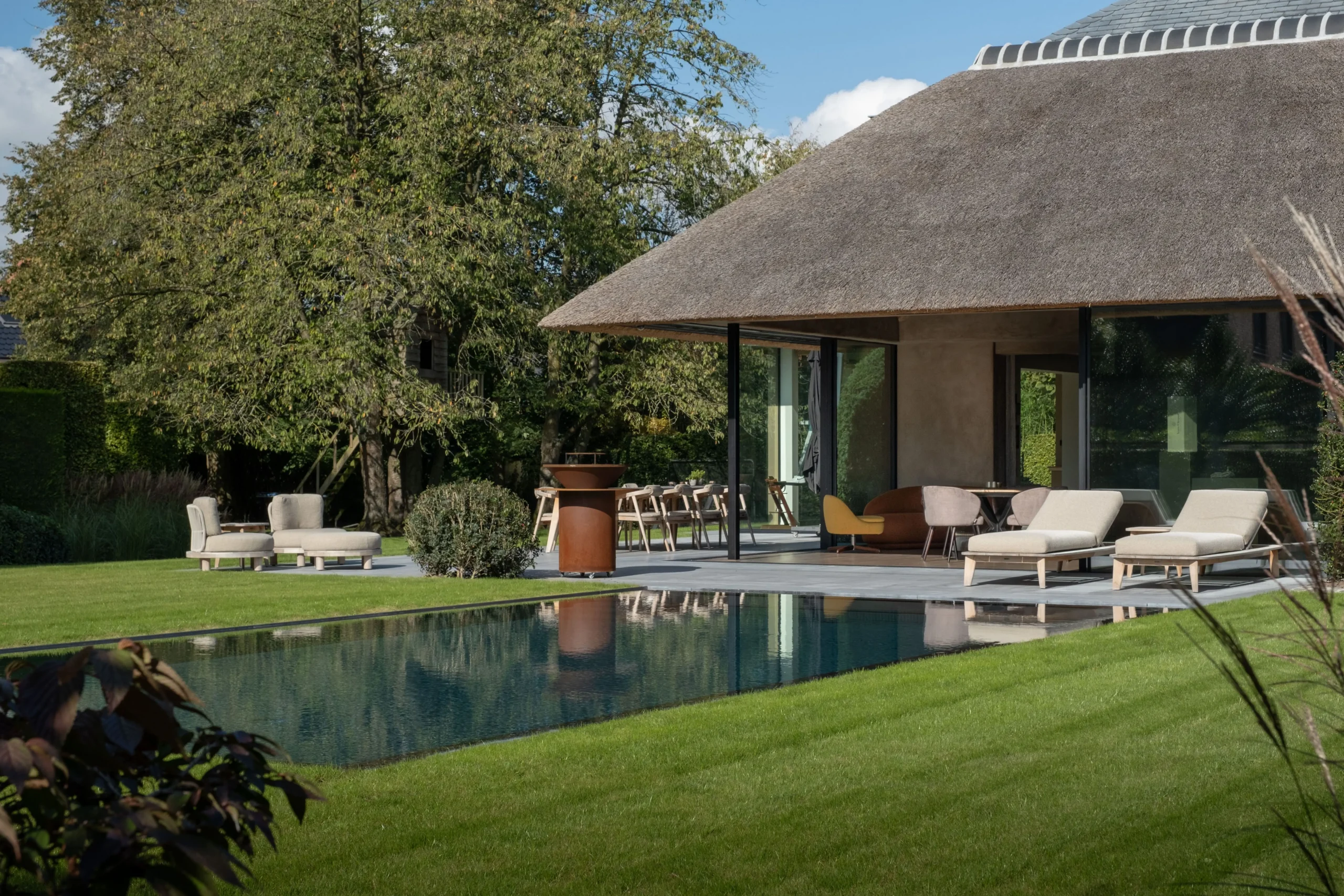 Poolhouse met rieten dak, geïntegreerd in een groene tuin met afgelijnd zwembad.