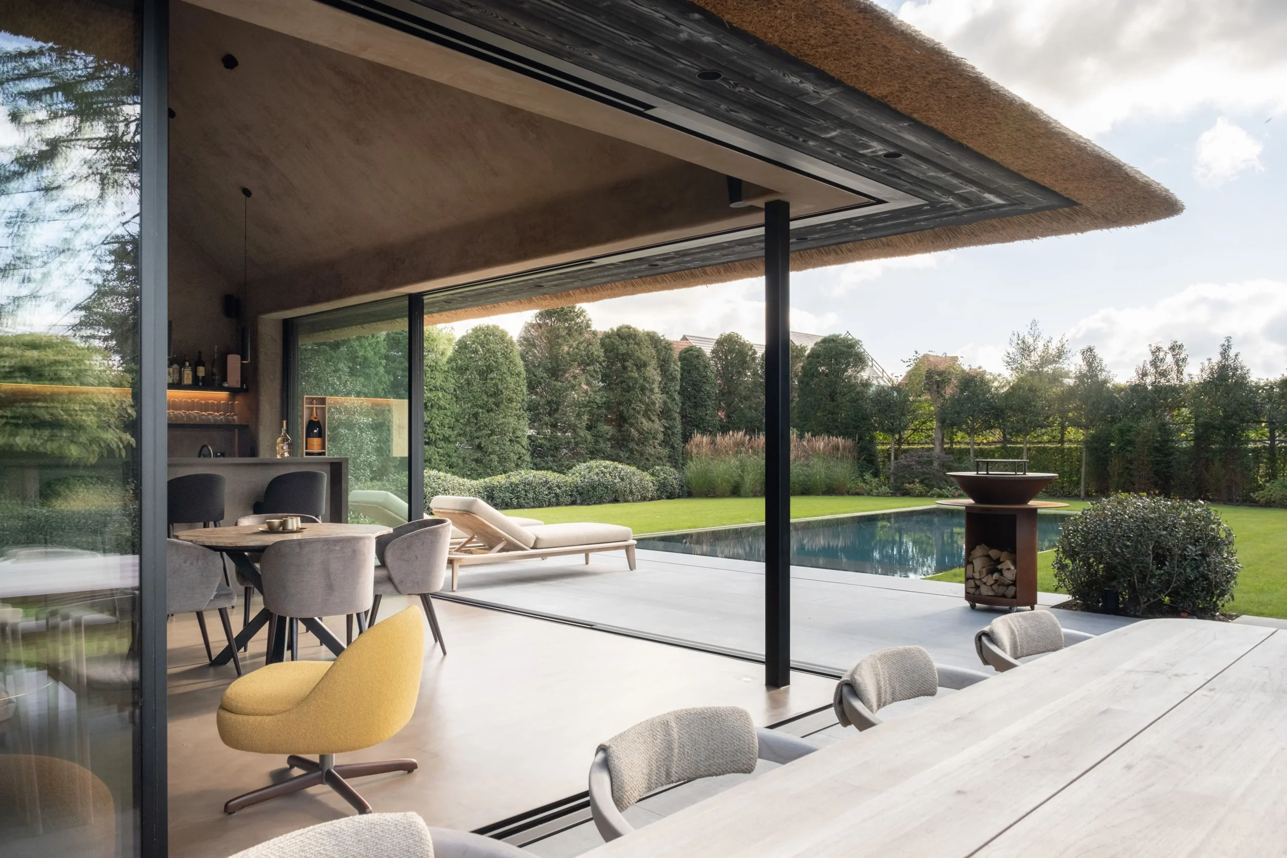 Overdekt terras met loungehoek en verbinding naar de tuin.