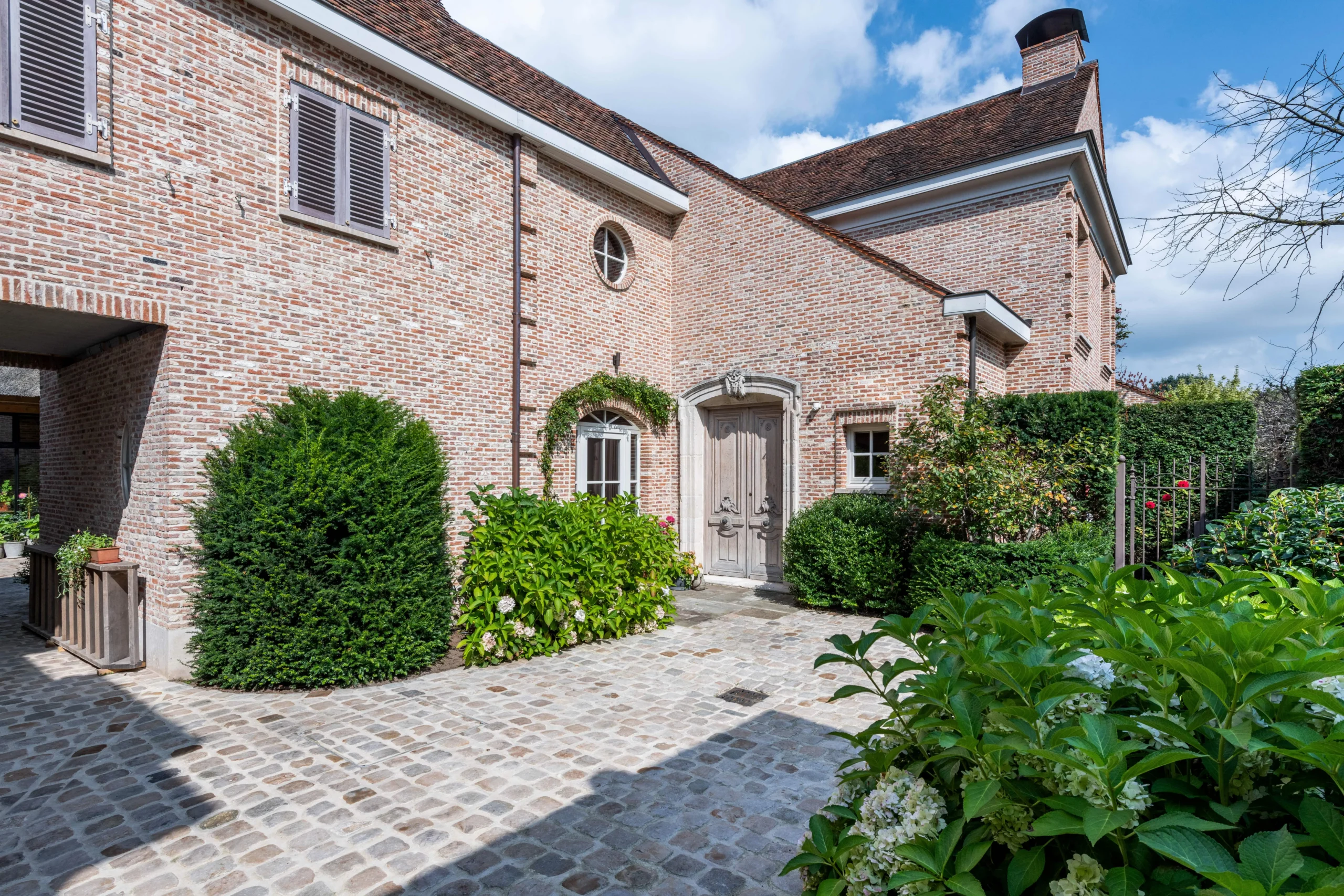 Landelijke woning met kasseien en groene omkadering.