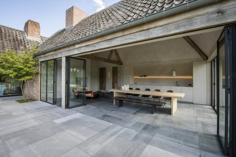 Overdekte eethoek met lange tafel en tuinzicht.