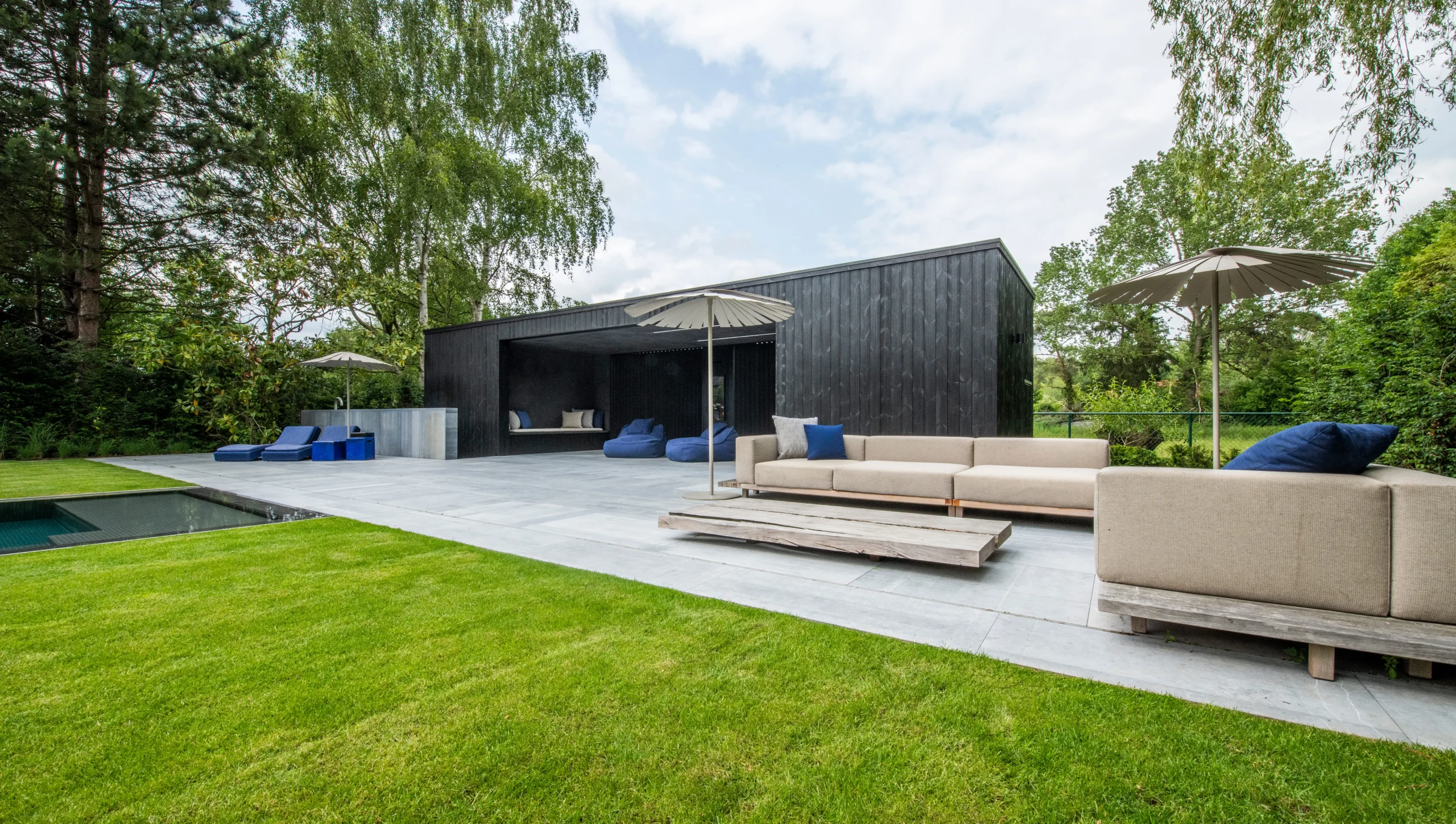 Loungeruimte met betonnen terras en groene tuin.