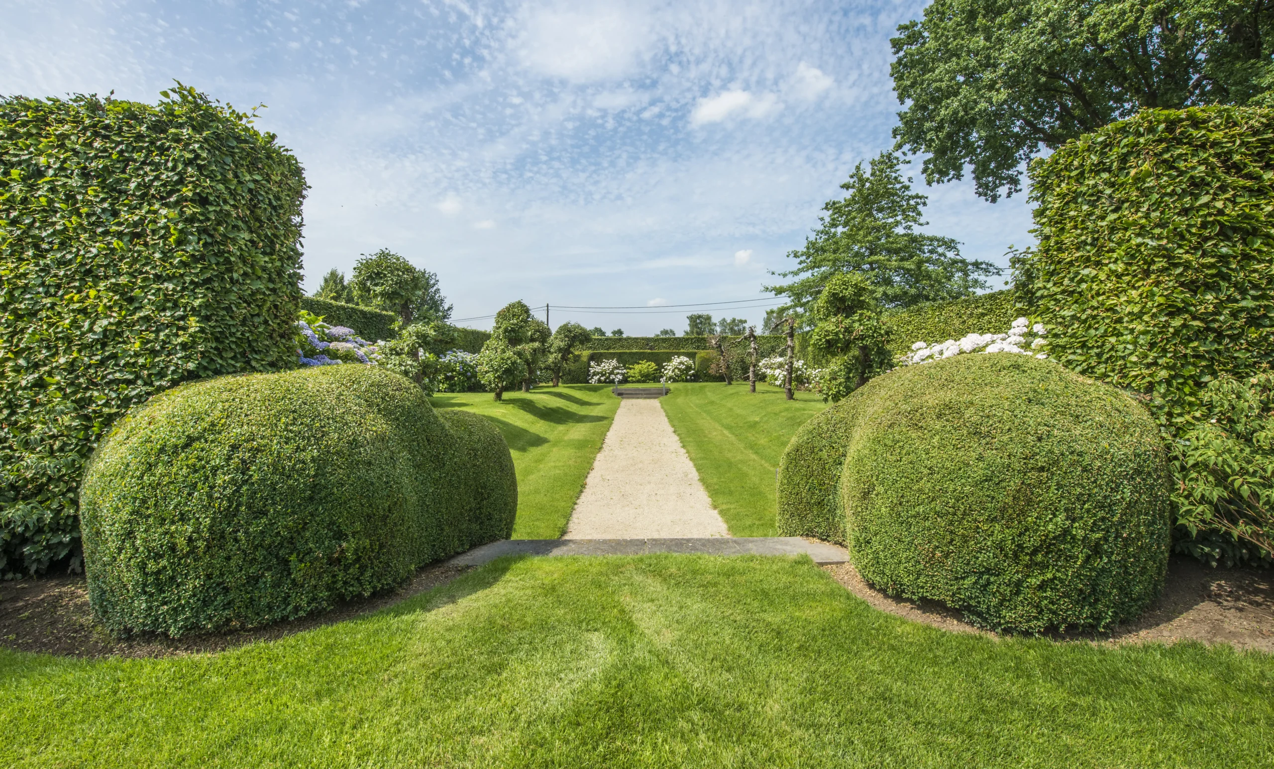 Tuinpad tussen hagen en open zicht op omliggend landschap.